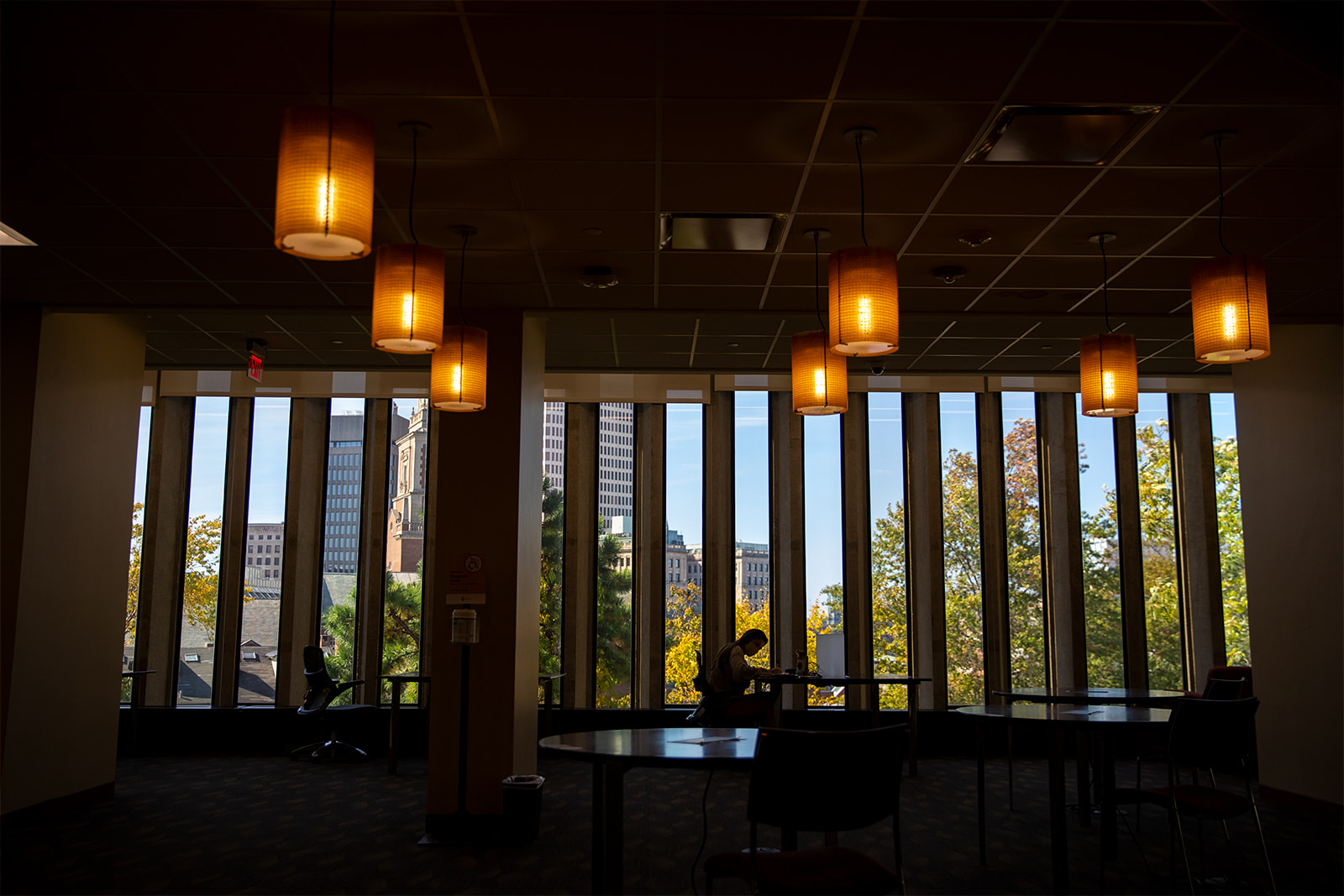 a person works at a desk by the window in the reading room of the Rockefeller Library. The person is in silhouette, and the room appears to be lit by lanterns.