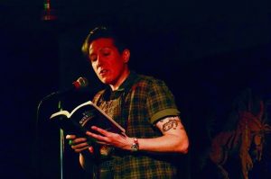 Megan Milks reading from a book at a microphone