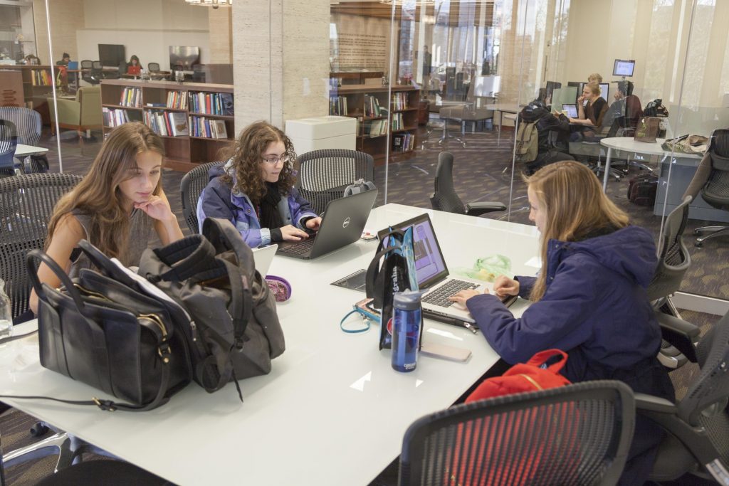 three students work on laptops at a table