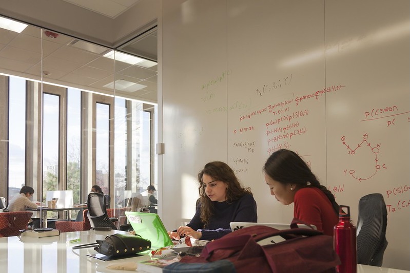 two students study in front of a white board with writing