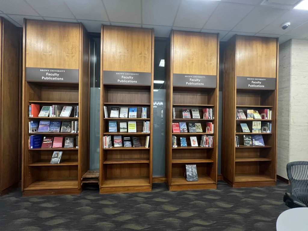 photo of four bookcases arrayed with books under signs on each bookcase that read Brown University Faculty Publications
