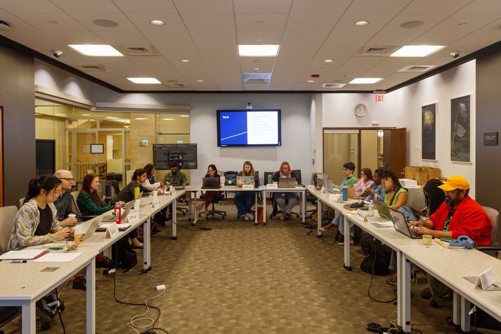 photo of people sitting around a U shaped conference table looking at laptops